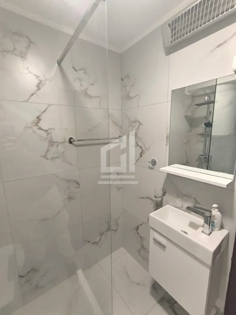 Small bathroom with a walk-in shower and a vanity with marble-patterned tiles.