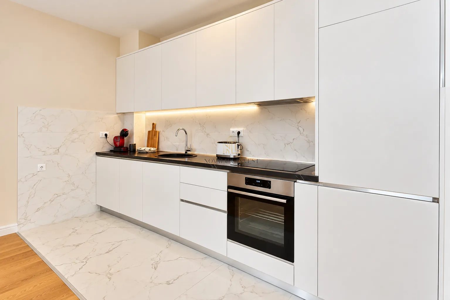 Modern white kitchen with built-in oven and marble-patterned tiles.