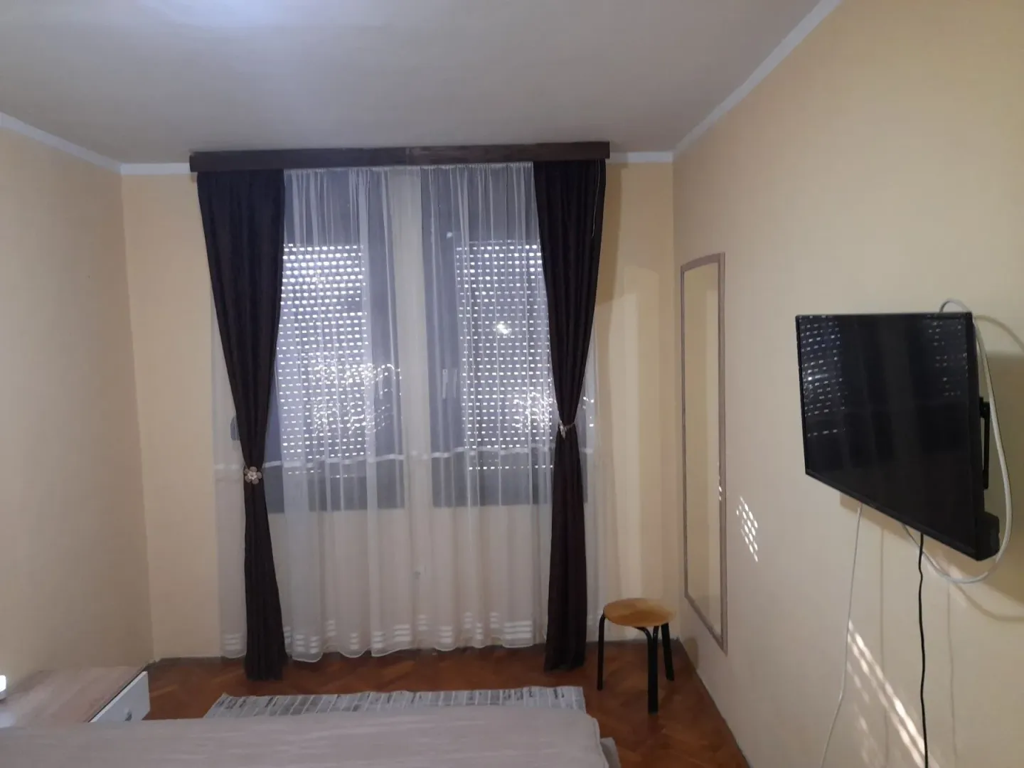 Spavaća soba sa televizorom na zidu i zavjesama na prozorima.