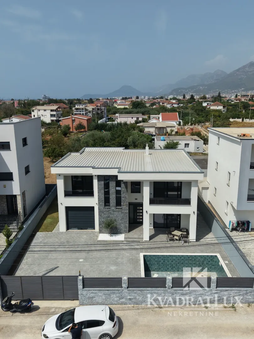 Pogled iz vazduha na modernu kuću sa dvorištem, bazenom i okruženjem.
