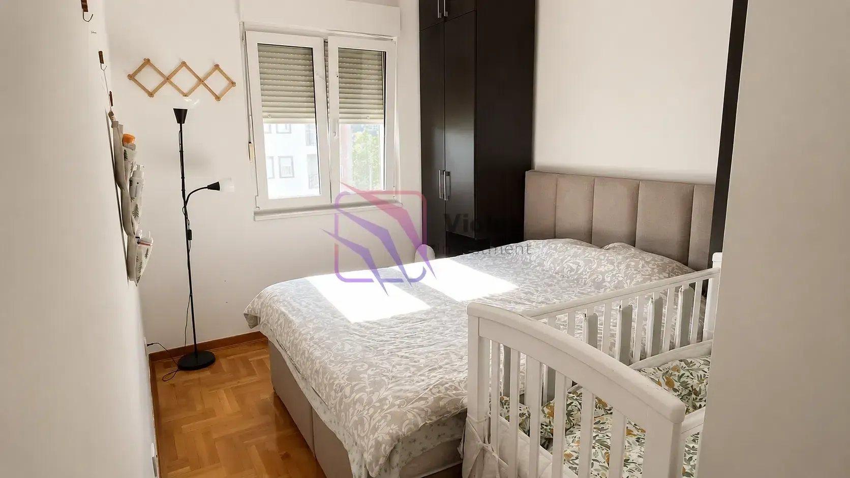 Spavaća soba sa bračnim krevetom, krevetcem i ormarom.