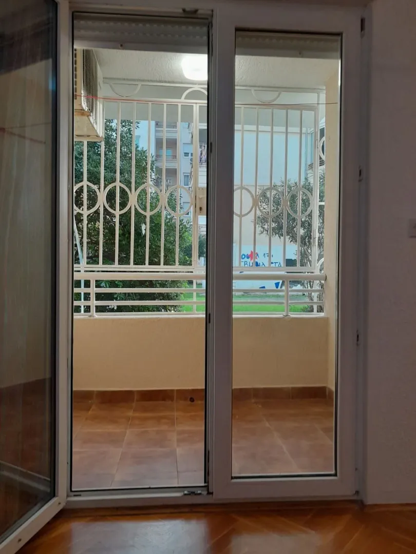 Pogled na popločani balkon sa zaštitnom rešetkom kroz otvorena vrata.