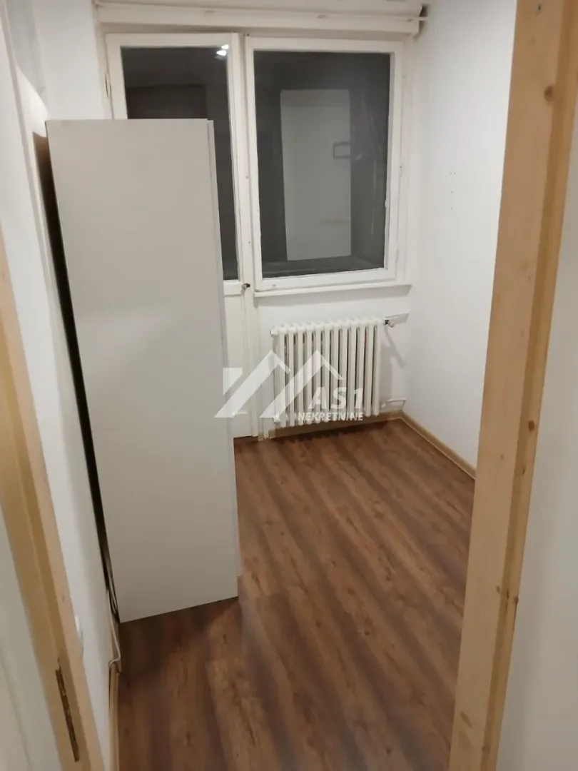 Small empty room with laminate flooring, white radiator, and balcony access.