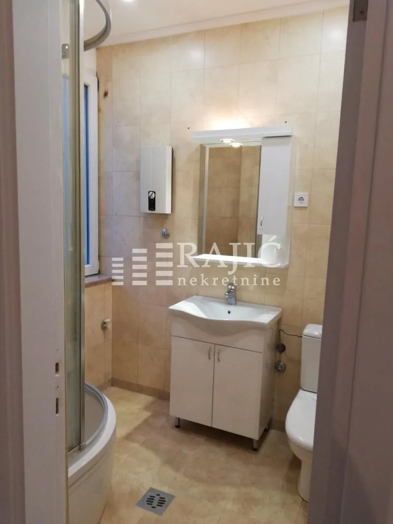 Smaller bathroom with a shower cabin, washbasin, and toilet.