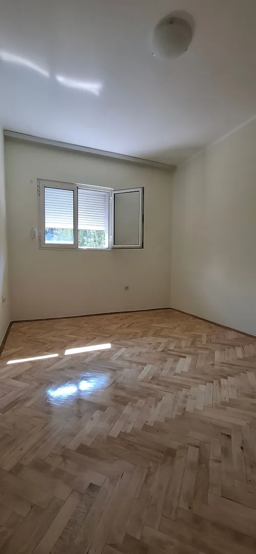 Prazna soba sa parketom i otvorenim prozorom.