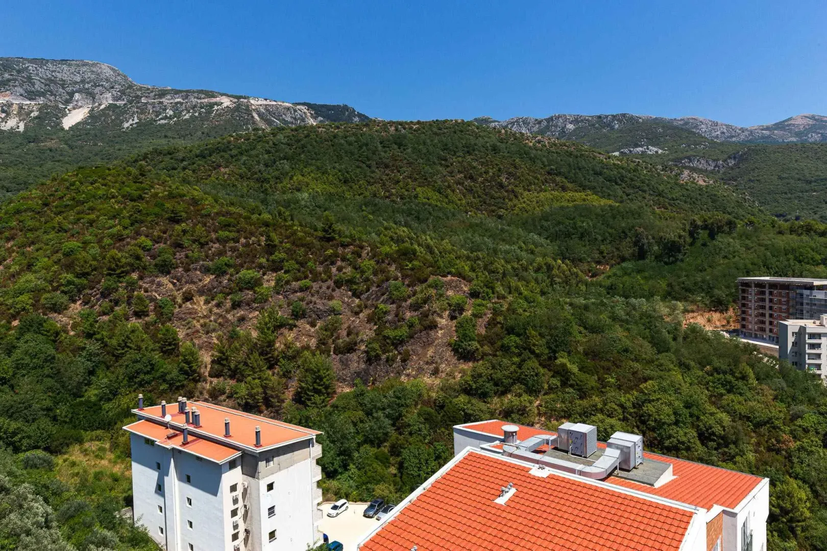 Pogled sa prozora na okolne zgrade, brda i šumu.