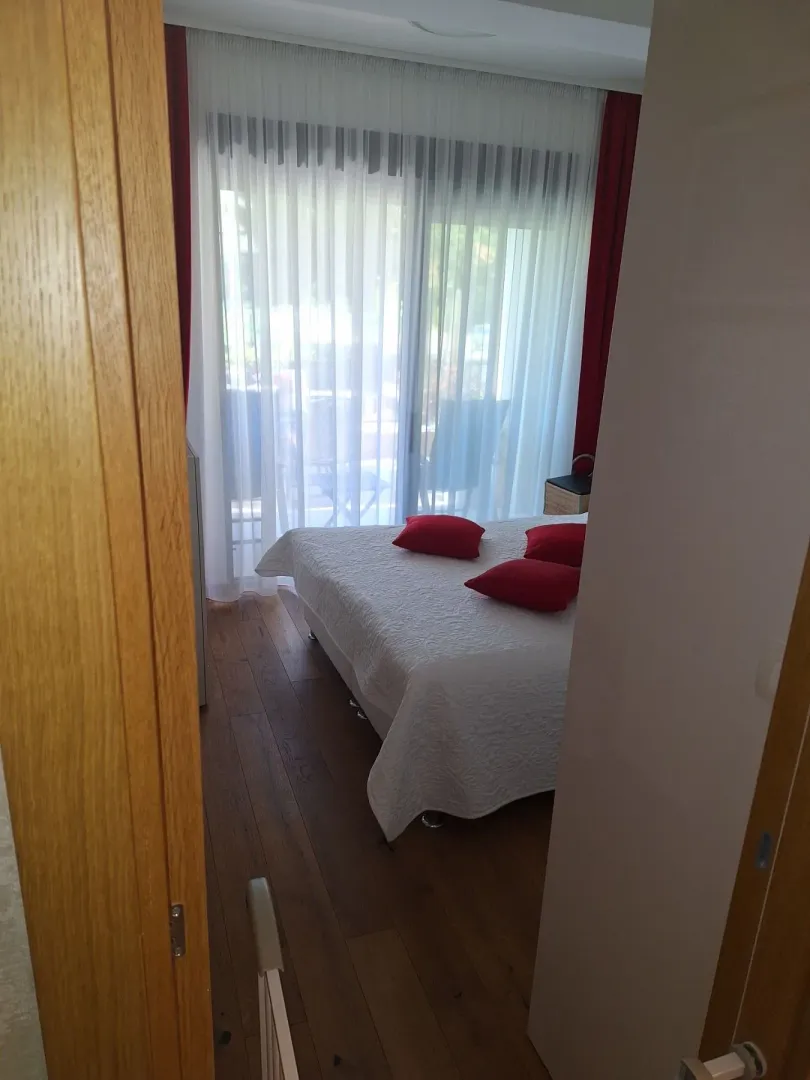 Pogled iz hodnika na spavaću sobu sa krevetom i balkonskim vratima.