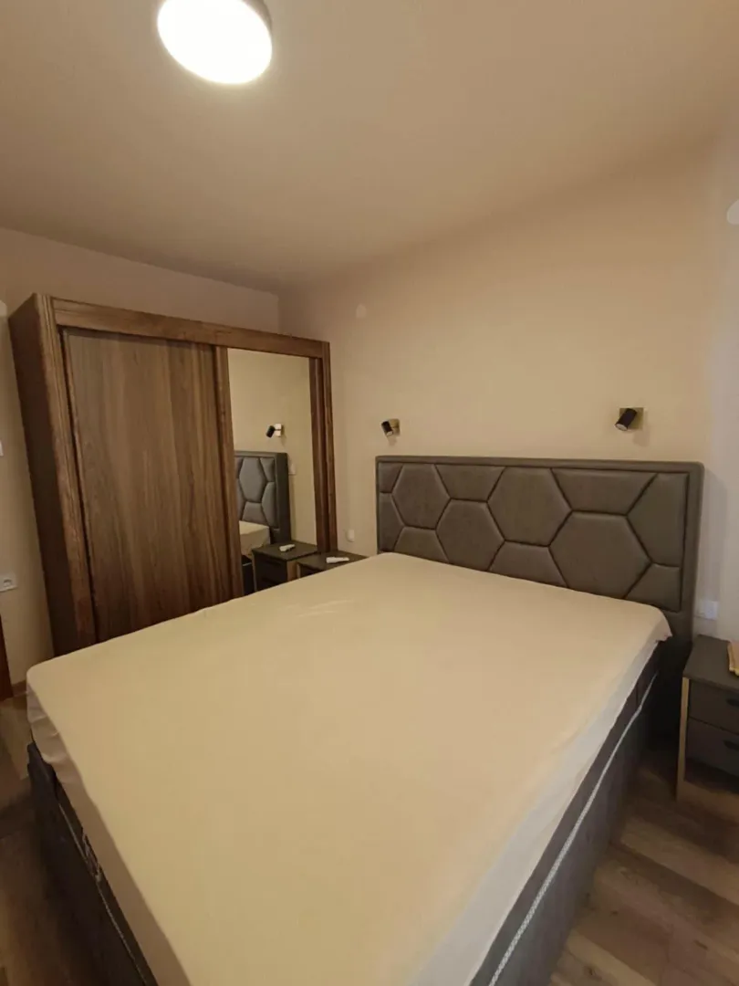 Spavaća soba sa bračnim krevetom, drvenim garderoberom i noćnim stočićima.