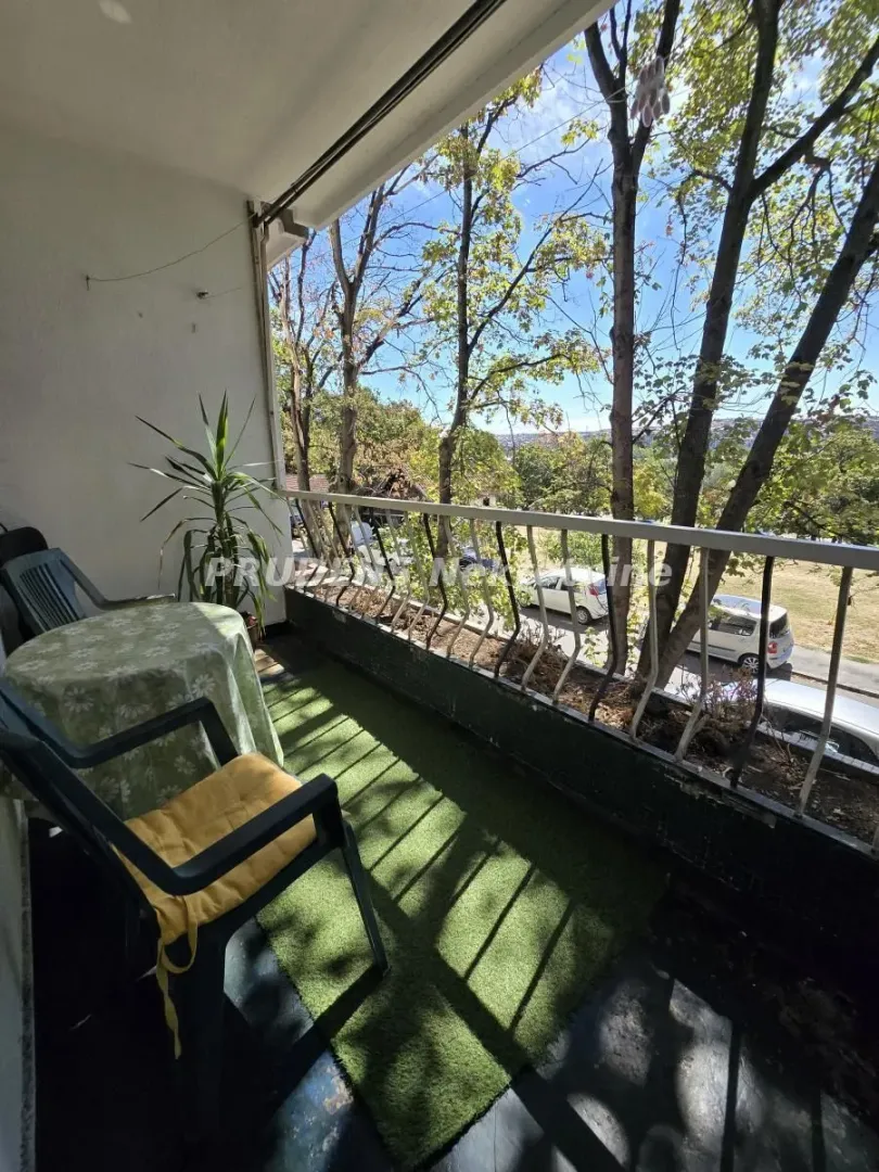 Natkriveni balkon sa garniturom za sedenje i pogledom na drveće.