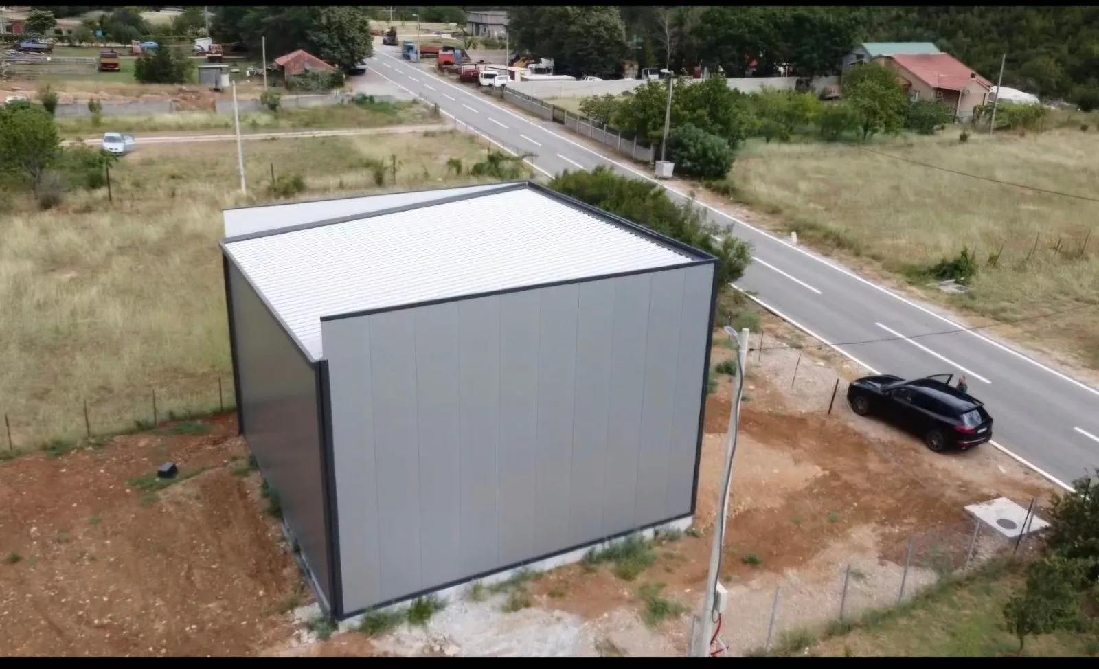 Aerial view of a modern prefabricated building and surrounding property next to the road.