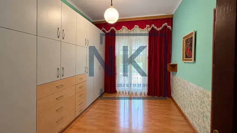 Bedroom with a large built-in wardrobe and balcony doors with red curtains.