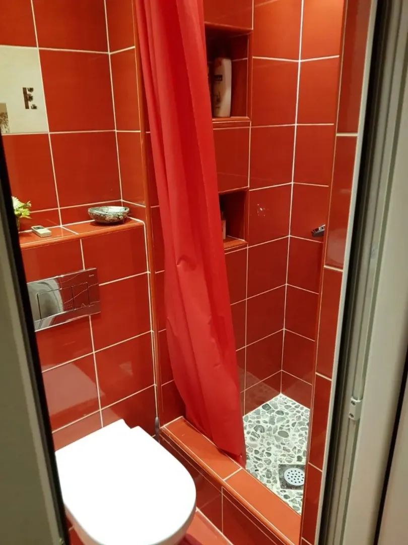 Kupatilo sa crvenim keramičkim pločicama i tuš kabinom sa zavjesom.