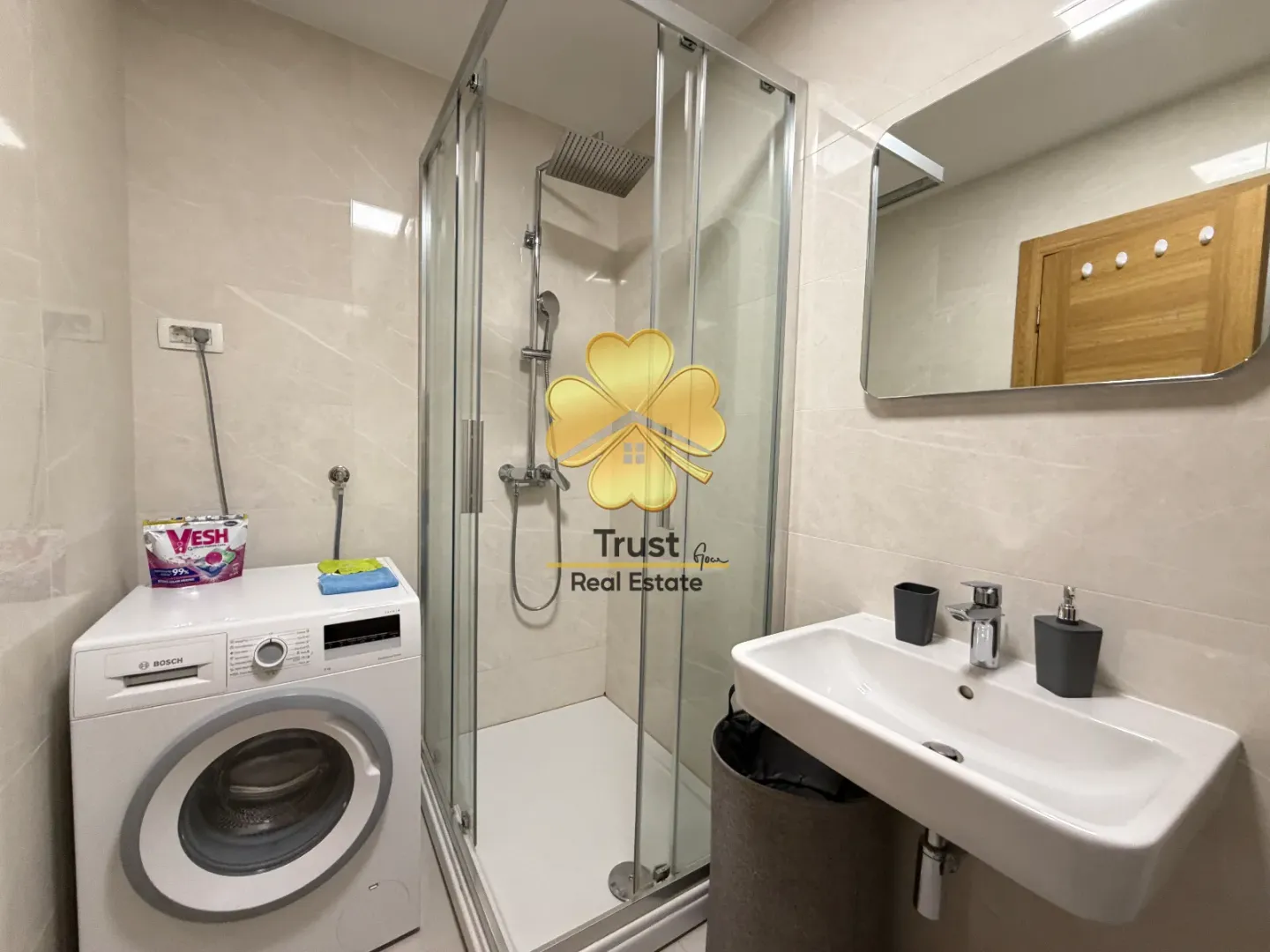 Modern bathroom with a shower cabin, washbasin, and washing machine.