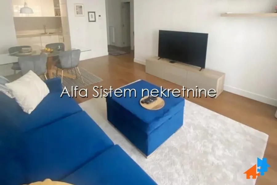 Dnevna soba sa garniturom, televizorom i trpezarijom u pozadini.