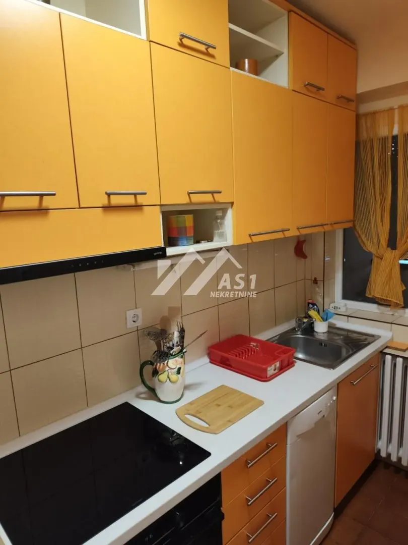 Kuhinja sa žutim elementima i ugradnom pločom i sudoperom.