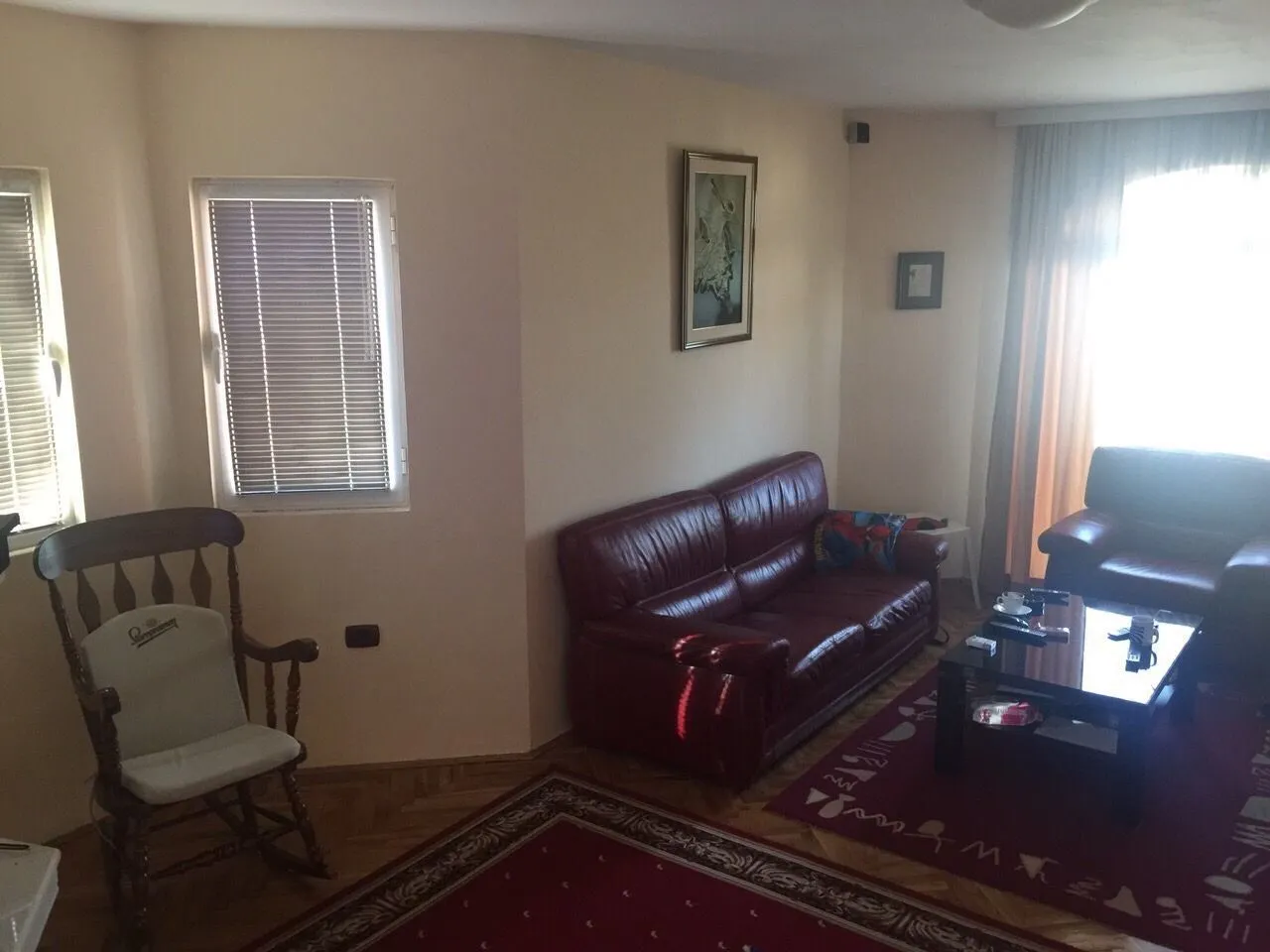 Living room featuring leather sofas, a wooden rocking chair, and red patterned carpets.