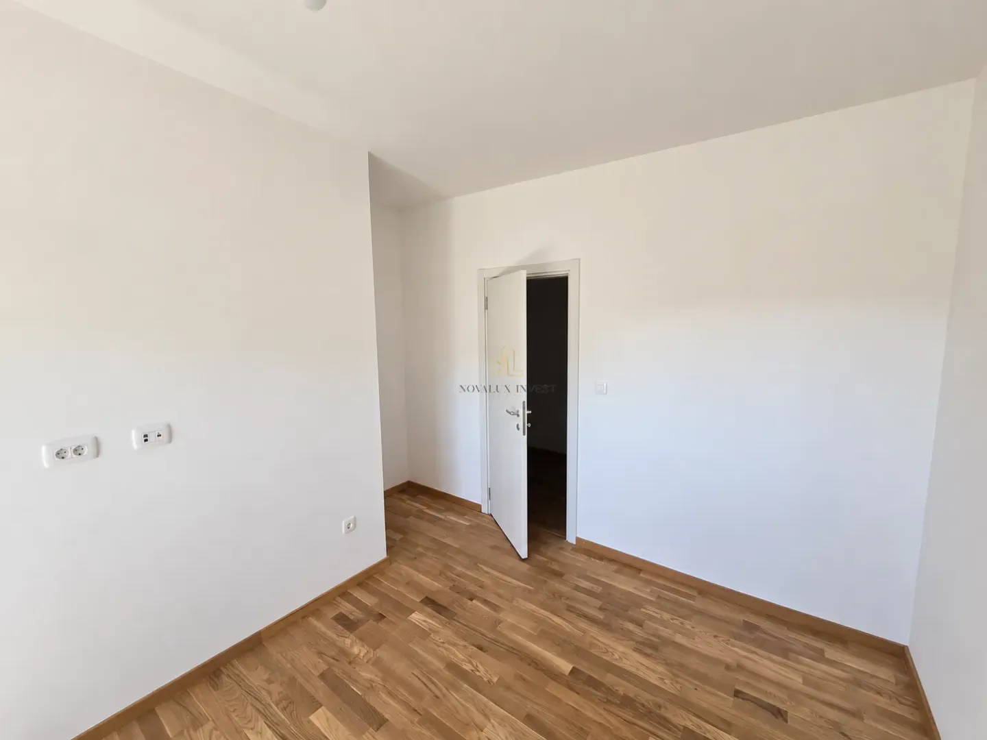 Prazna prostorija sa bijelim zidovima i drvenim podom.