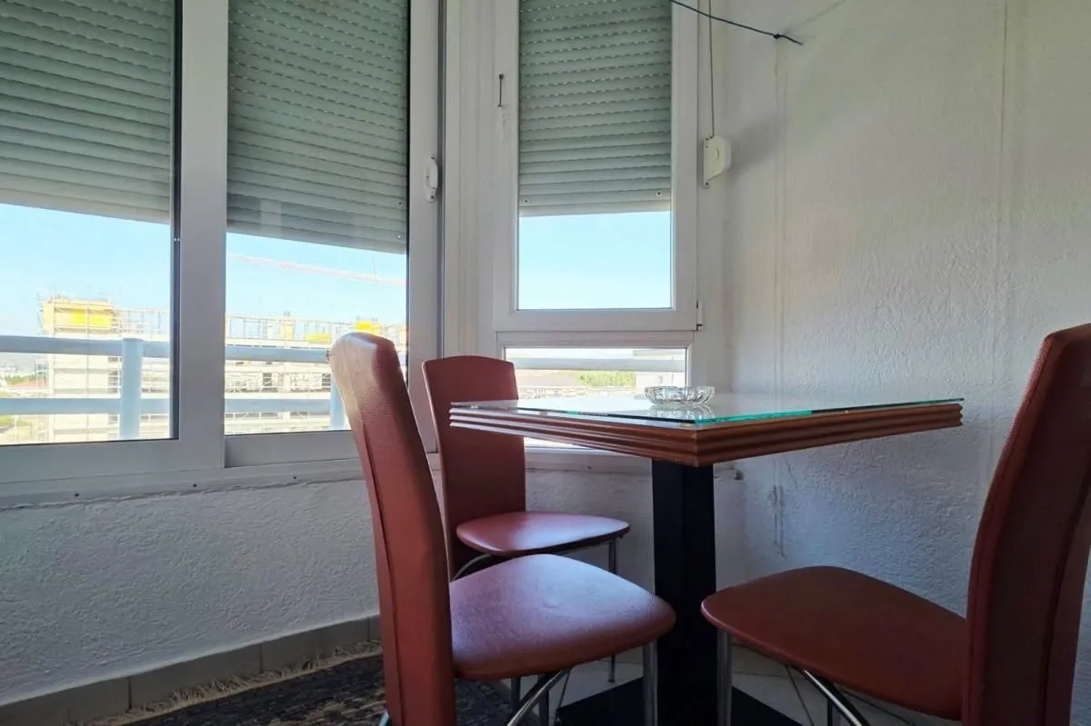 Zastakljeni balkon sa malim stolom i crvenim stolicama.