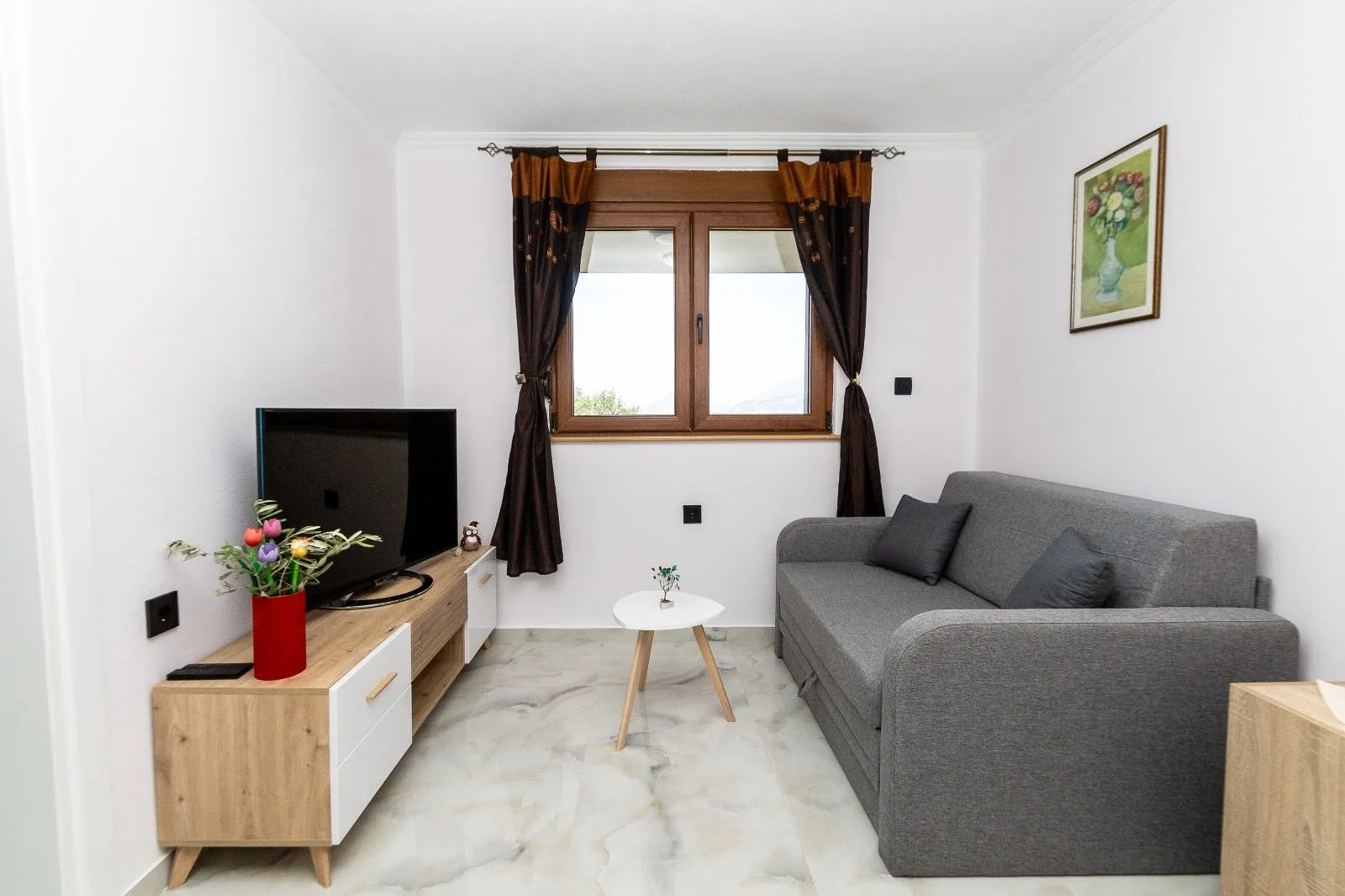 Small living room with a grey sofa, TV unit, and window.