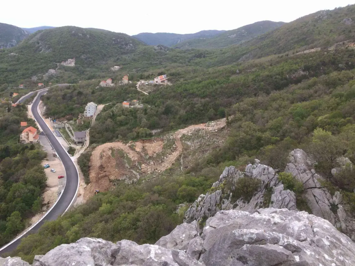 Pogled na brdoviti krajolik, put i okolne kuće.