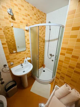 Manje kupatilo obloženo narandžastim i bijelim pločicama sa tuš kabinom i umivaonikom. - image 4