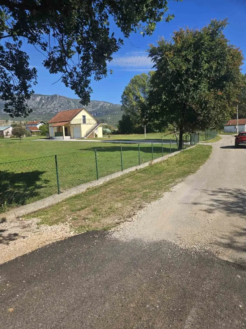 Jednospratna kuća sa prostranim dvorištem i ogradom pored lokalnog puta.