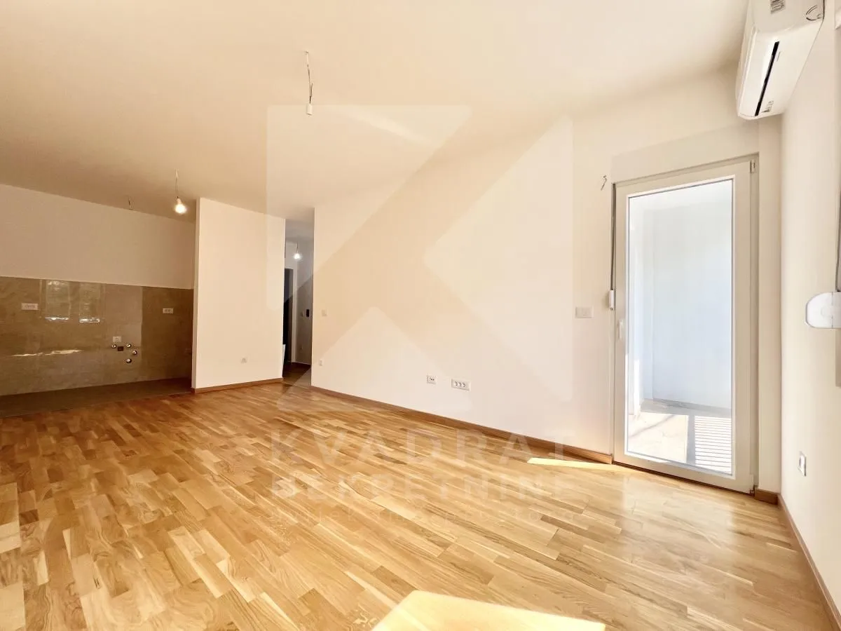 Empty living room with wooden flooring and access to the terrace.