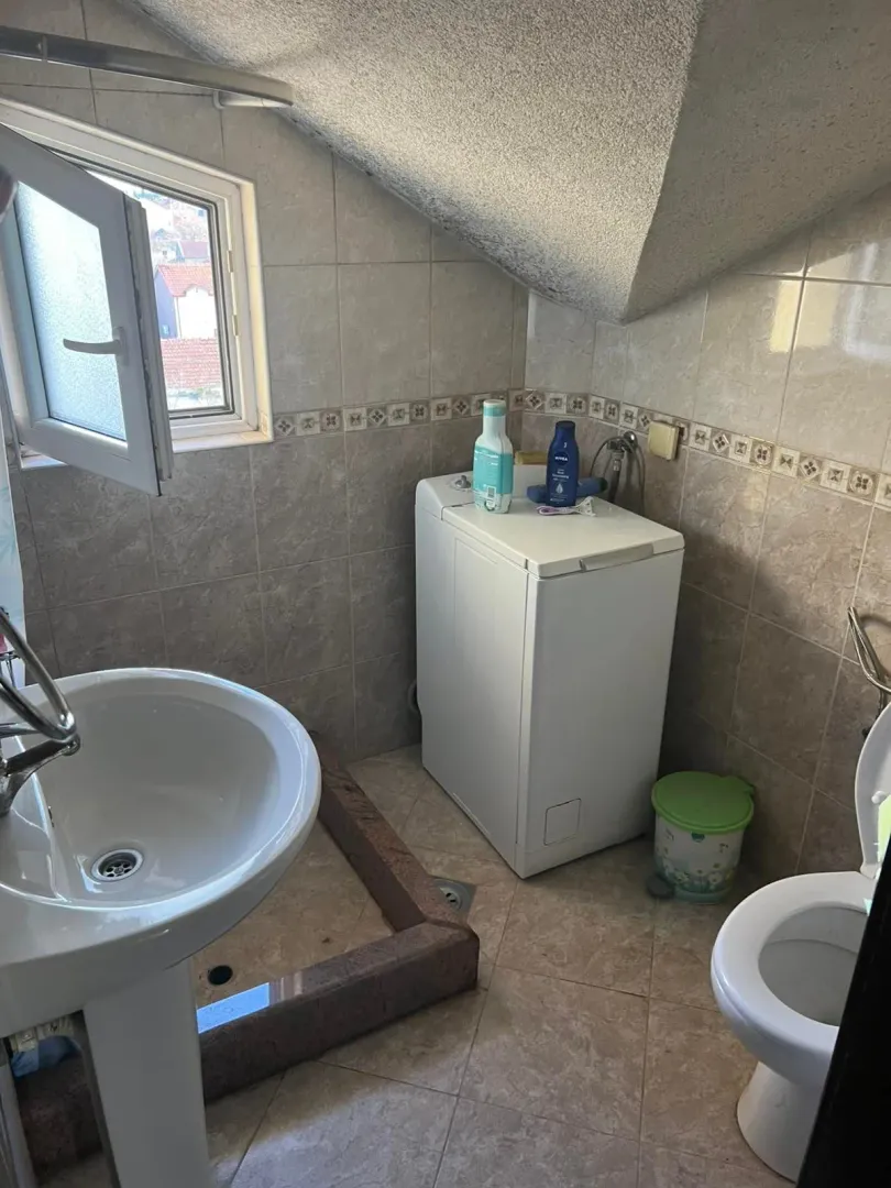 Kupatilo sa umivaonikom, veš mašinom, wc šoljom i prozorom pod krovnim kosinama.