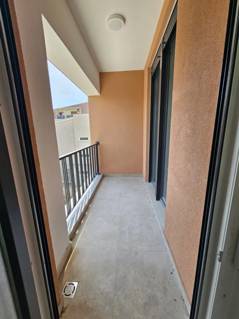 Prazan natkriveni balkon sa pločicama i crnom ogradom.