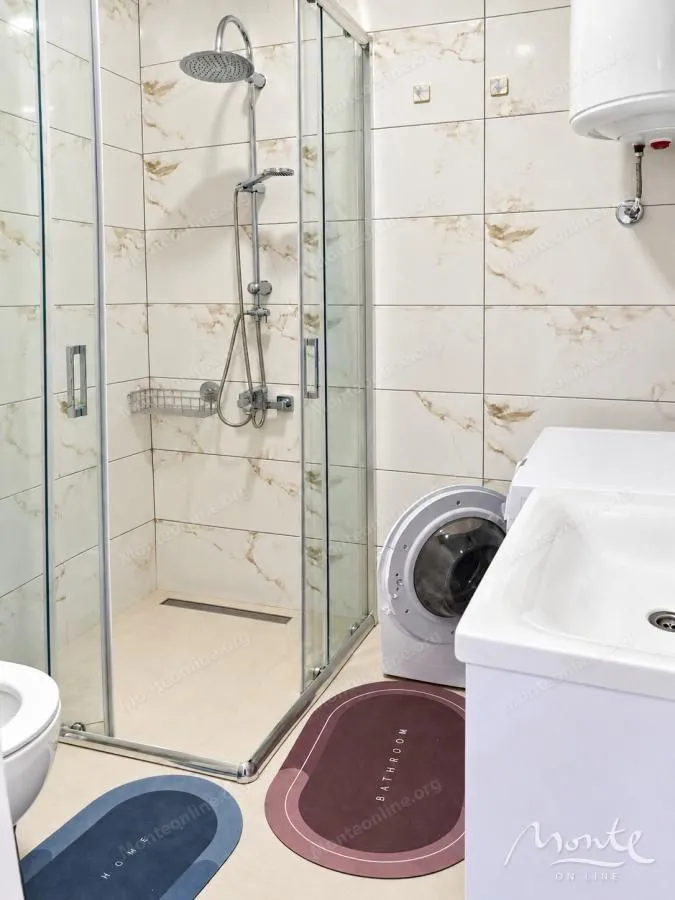 Kupatilo opremljeno tuš kabinom, umivaonikom i veš mašinom.