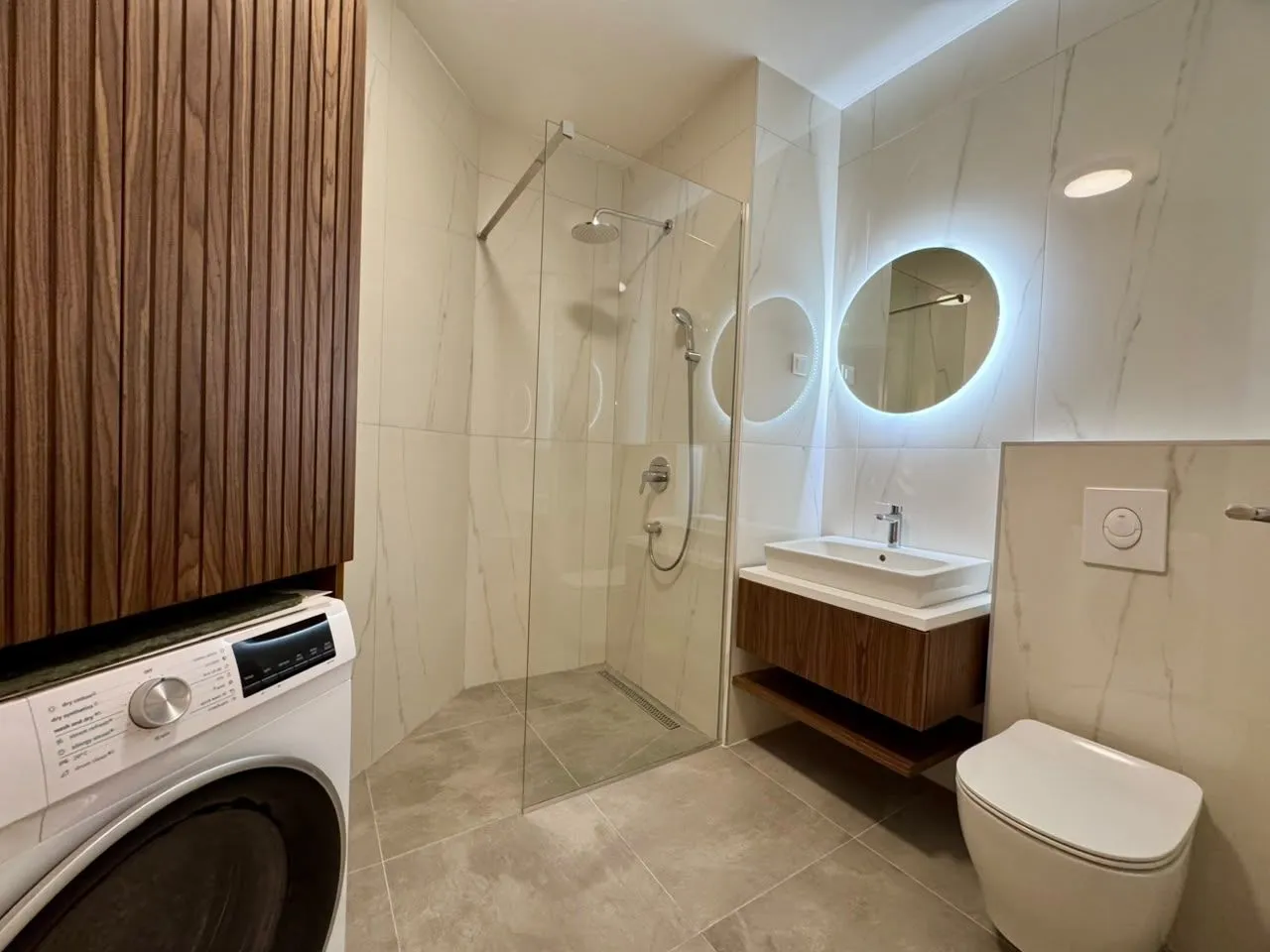 Modern bathroom with a walk-in shower, washbasin, and washing machine.