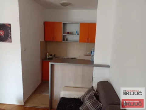 Manja kuhinja sa narandžastim elementima i šankom povezana sa dnevnim boravkom. - image 5