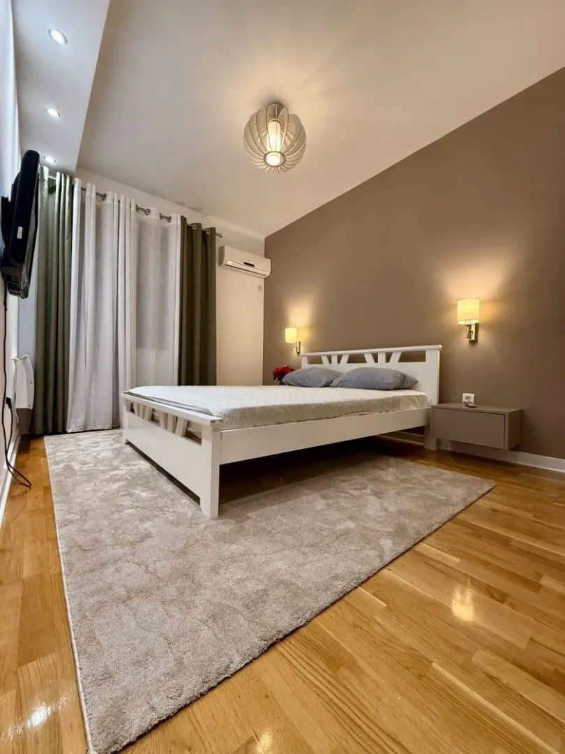A furnished bedroom with a double bed, a rug, and hardwood flooring.