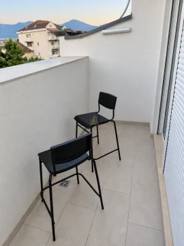 A small tiled balcony with two black bar stools and a view of surrounding buildings and hills. - image 7