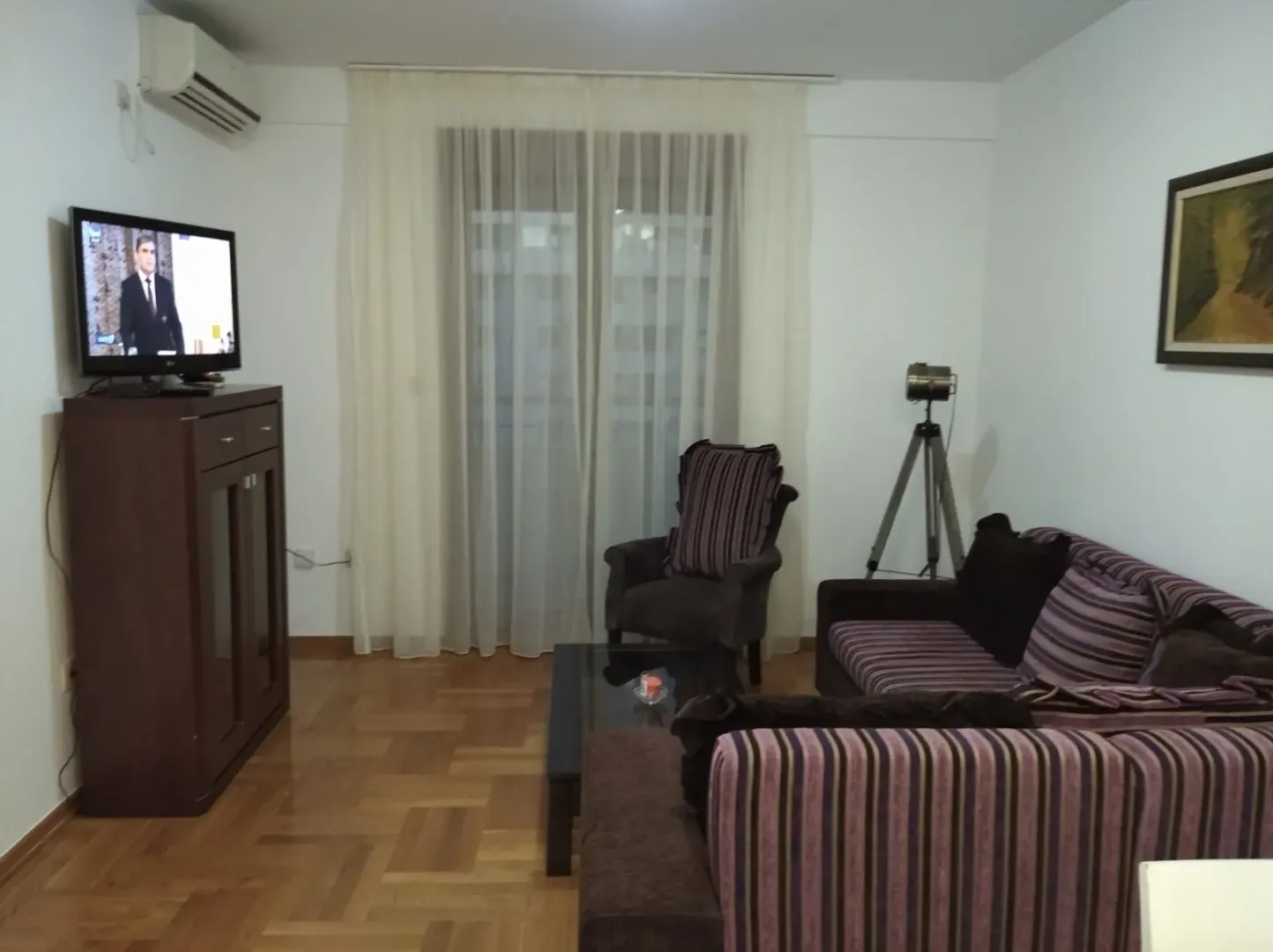 Dnevna soba sa garniturom, televizorom i drvenim podom.