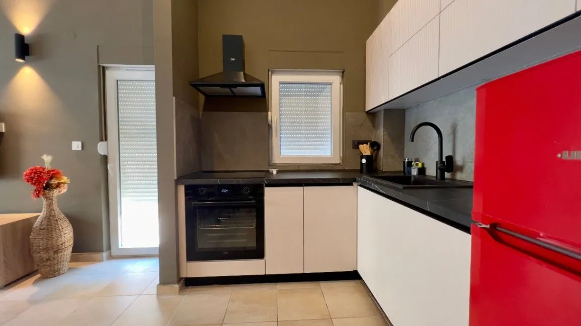 Modern kitchen equipped with white cabinets, dark countertop, and a red refrigerator.