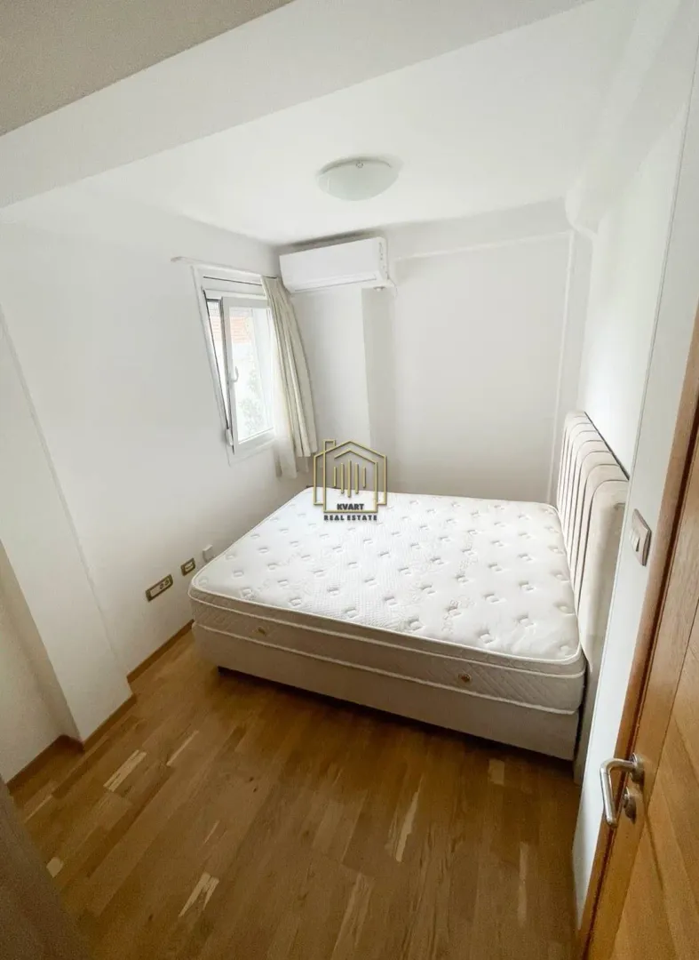 Small bedroom with a double bed, wooden floor, and air conditioning unit.