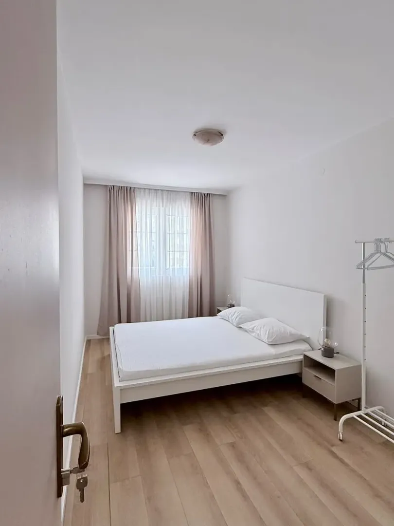 Bright bedroom with a white bed and parquet flooring.