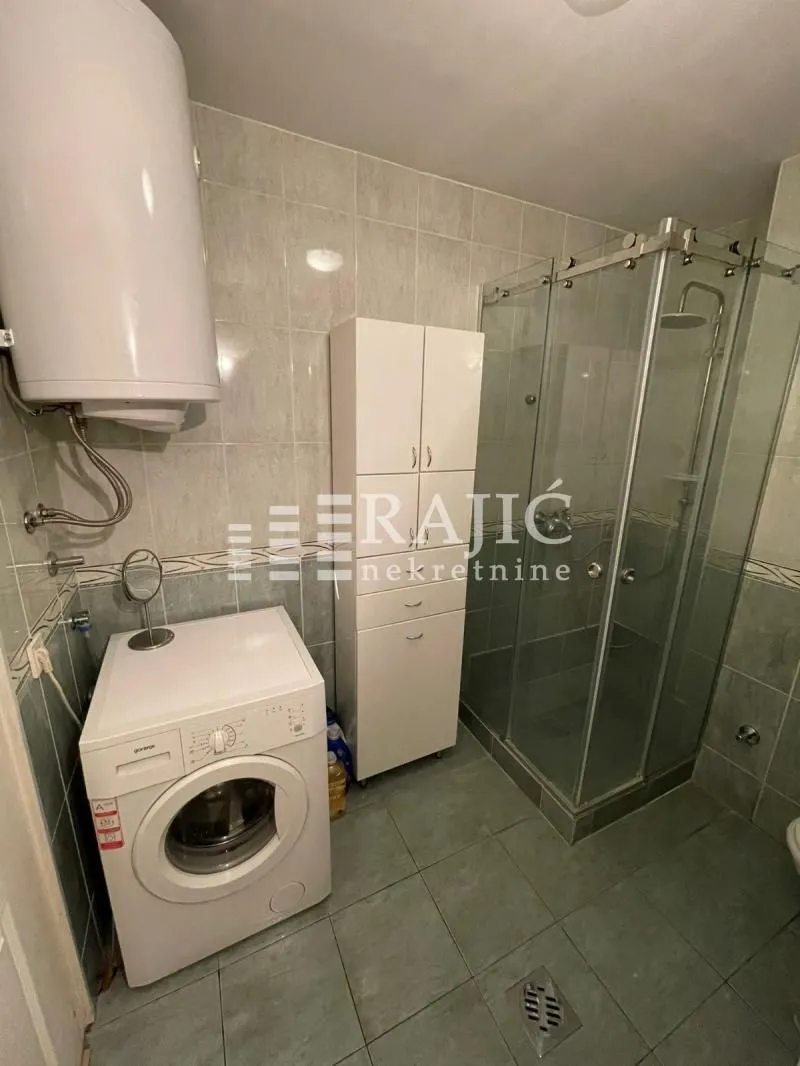 Bathroom with a shower cabin, cabinet, water heater, and washing machine.
