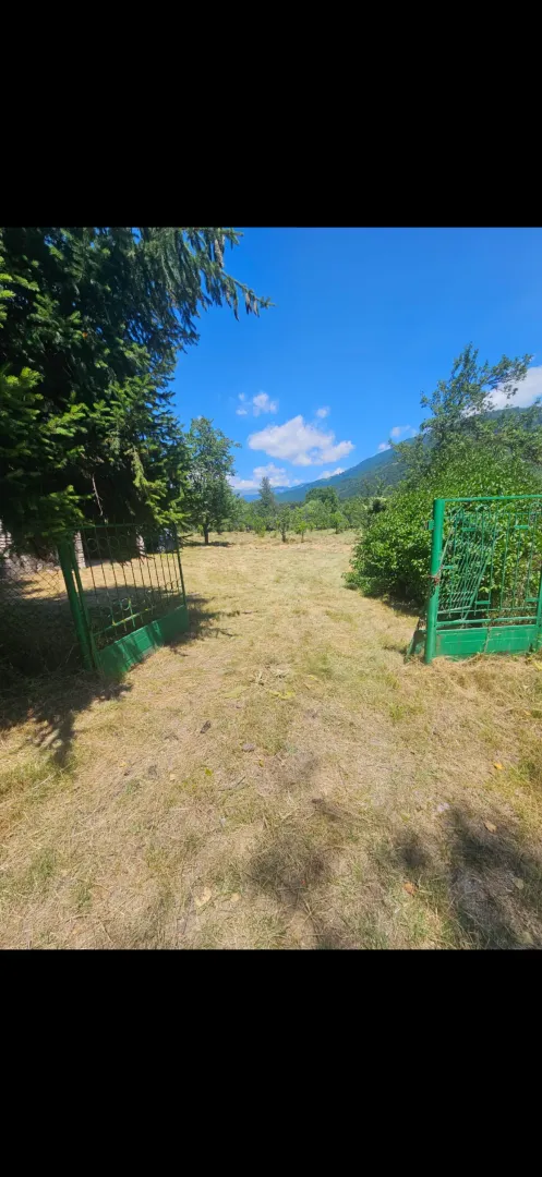 Ograđeno dvorište sa zelenom kapijom i pogledom na prirodu i planine.