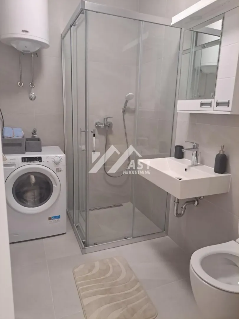 Modern bathroom with a shower cabin, washbasin, toilet, and washing machine.