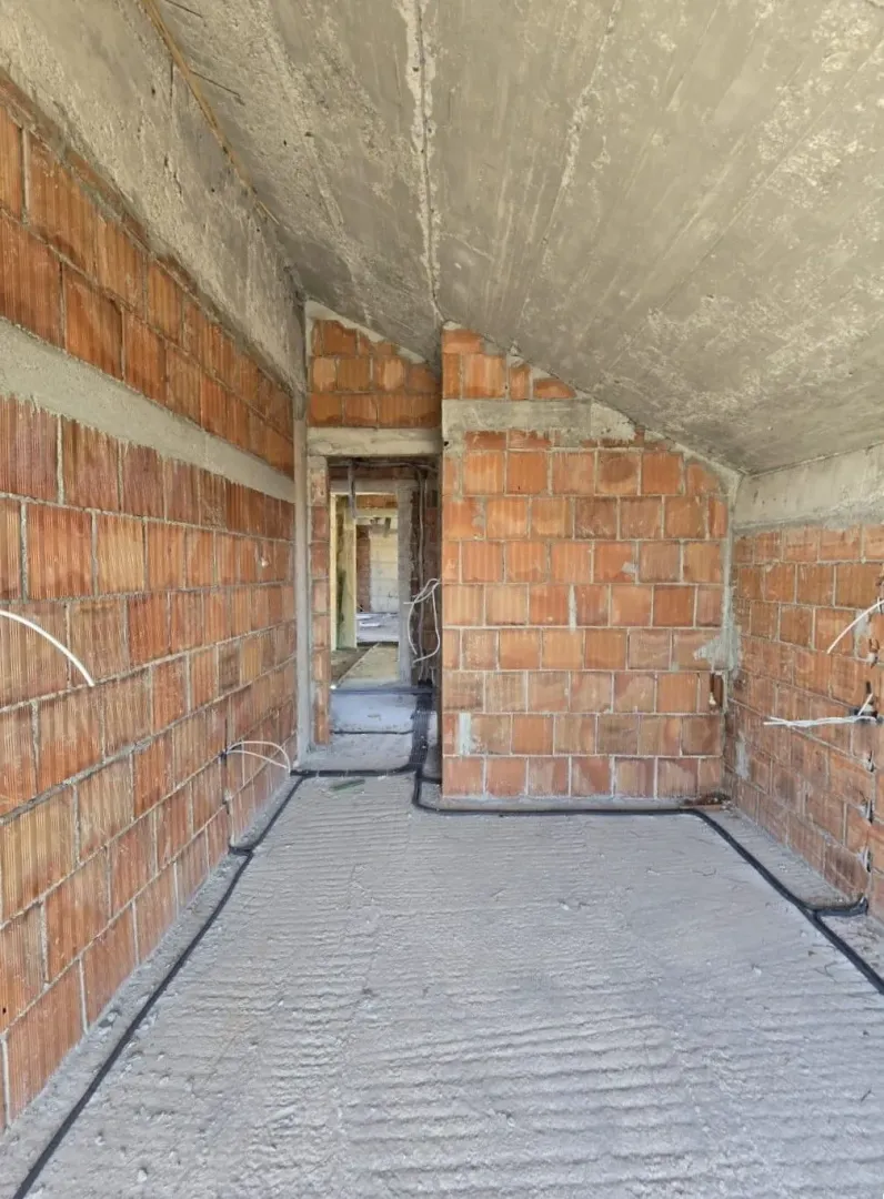 Unutrašnjost prostorije u izgradnji sa golim ciglama i betonskim plafonom.