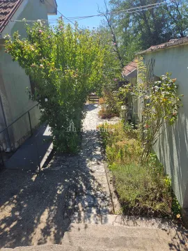 Popločana staza u dvorištu okružena zelenilom i drvećem. - image 3
