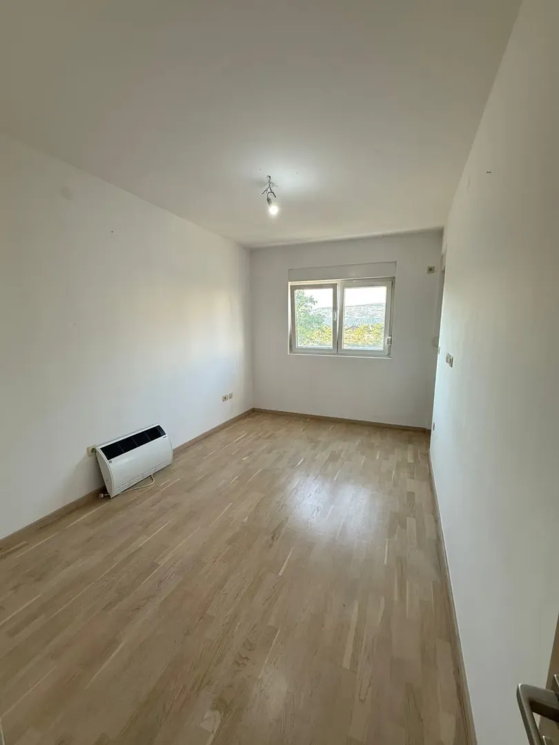Prazna soba sa bijelim zidovima, parketom i klima uređajem.