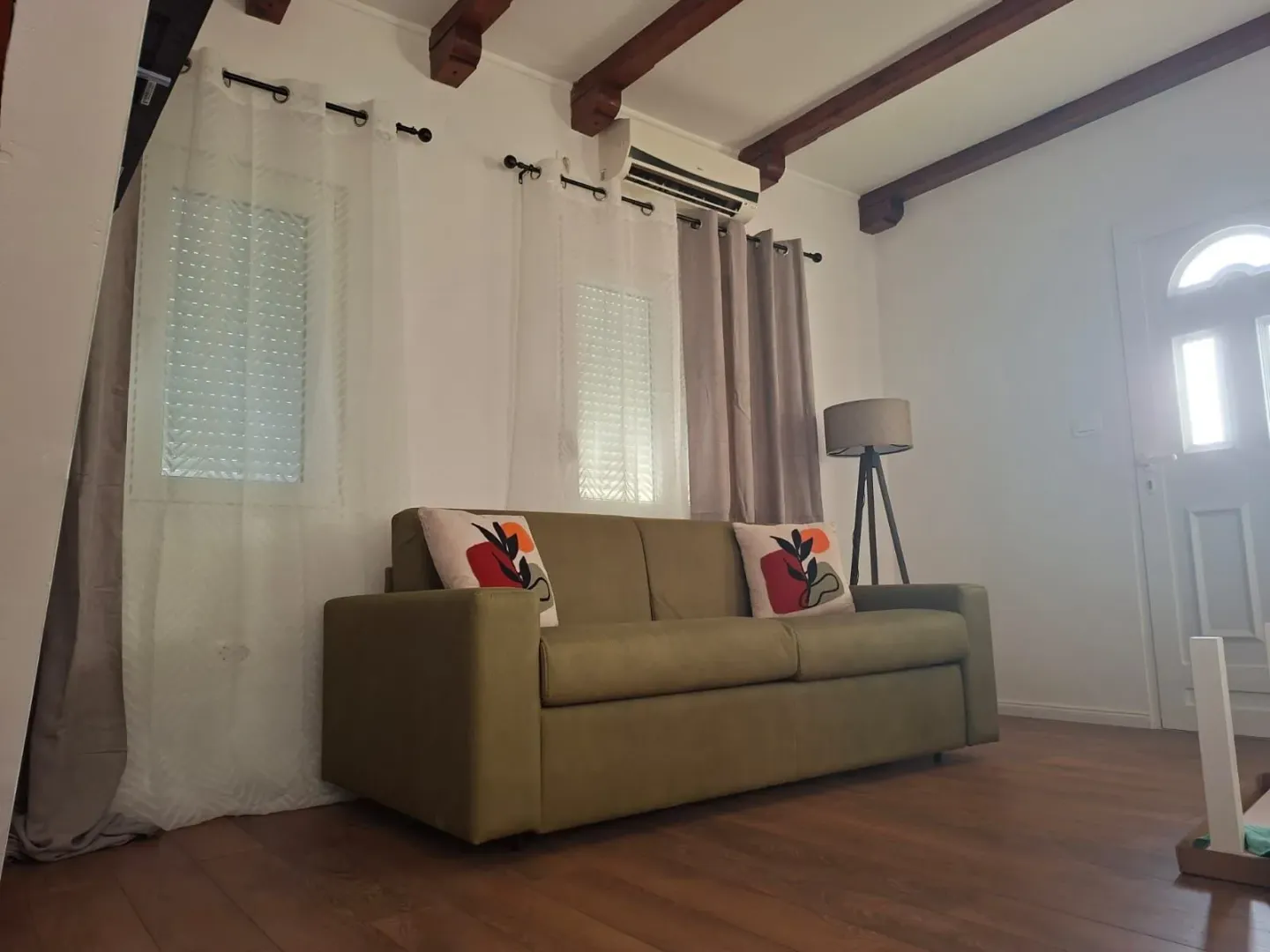 Living room with a green sofa and wooden ceiling beams.