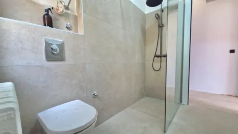 Moderno kupatilo sa tuš kabinom i ugradnom šoljom obloženo keramičkim pločicama. - image 7
