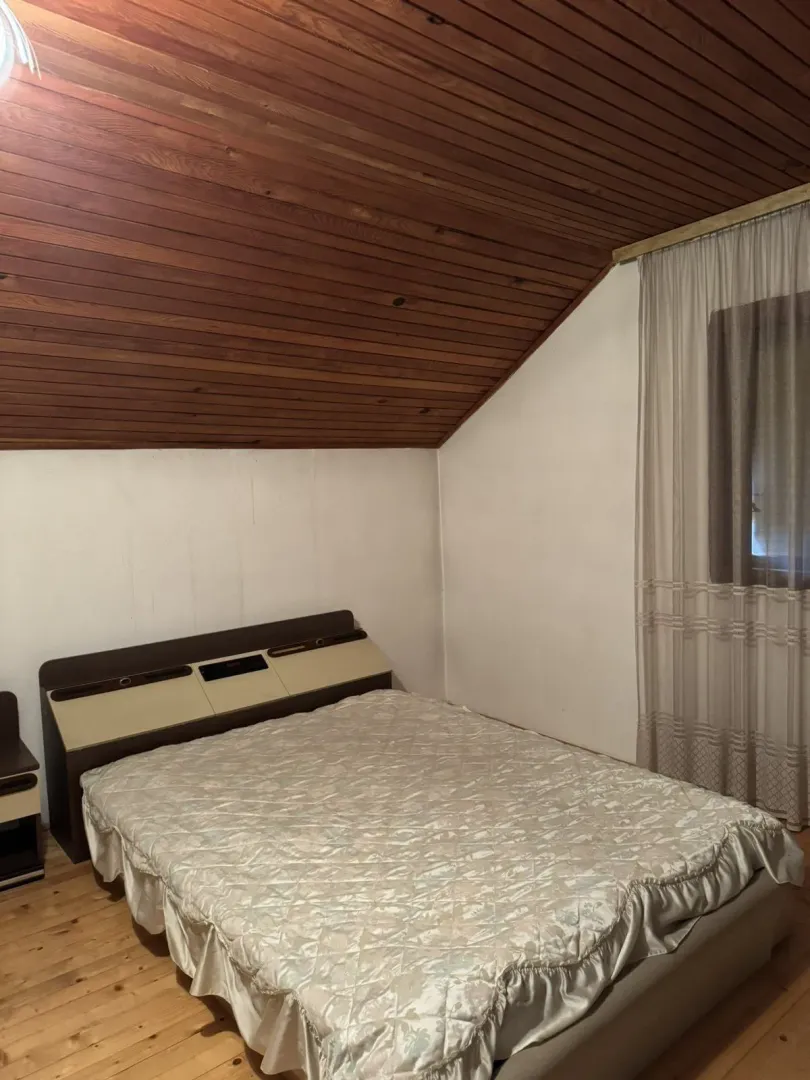 Jednostavna spavaća soba sa kosim drvenim plafonom i bračnim krevetom.