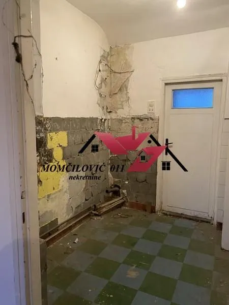 Stara kuhinja u procesu renoviranja sa ogoljenim zidovima i keramičkim pločicama na podu.