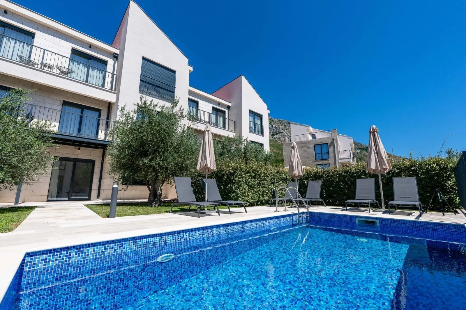 Swimming pool in front of the residential building with sun loungers and umbrellas.