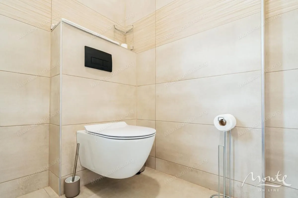 Moderno opremljeno kupatilo sa konzolnom wc šoljom i bež pločicama.